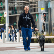 Salesforce Trailblazer, smiling and walking across the street with his guide dog