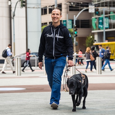 Salesforce Trailblazer, smiling and walking with his guide dog